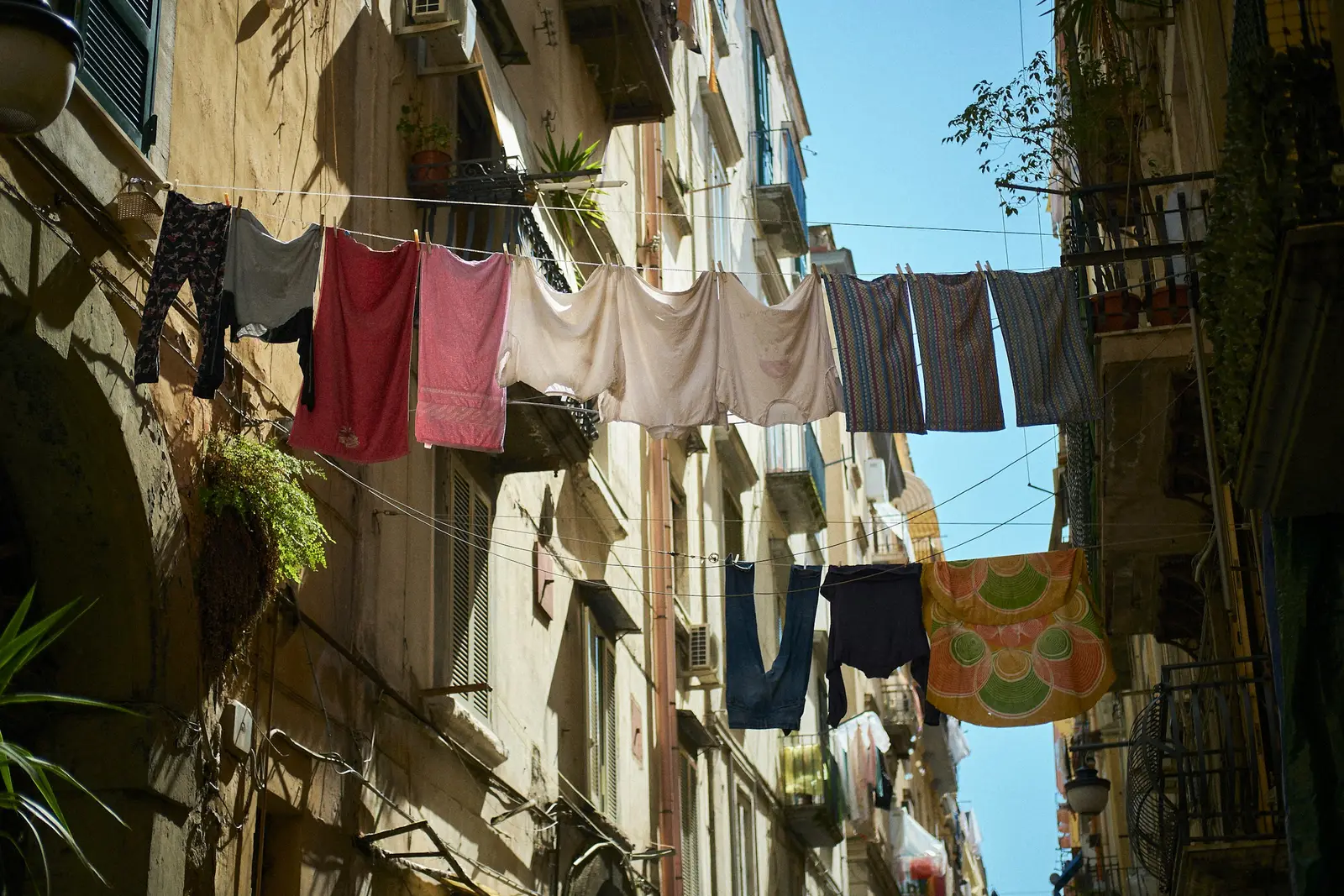 A sunny narrow street in Naples with laundry hanging between buildings