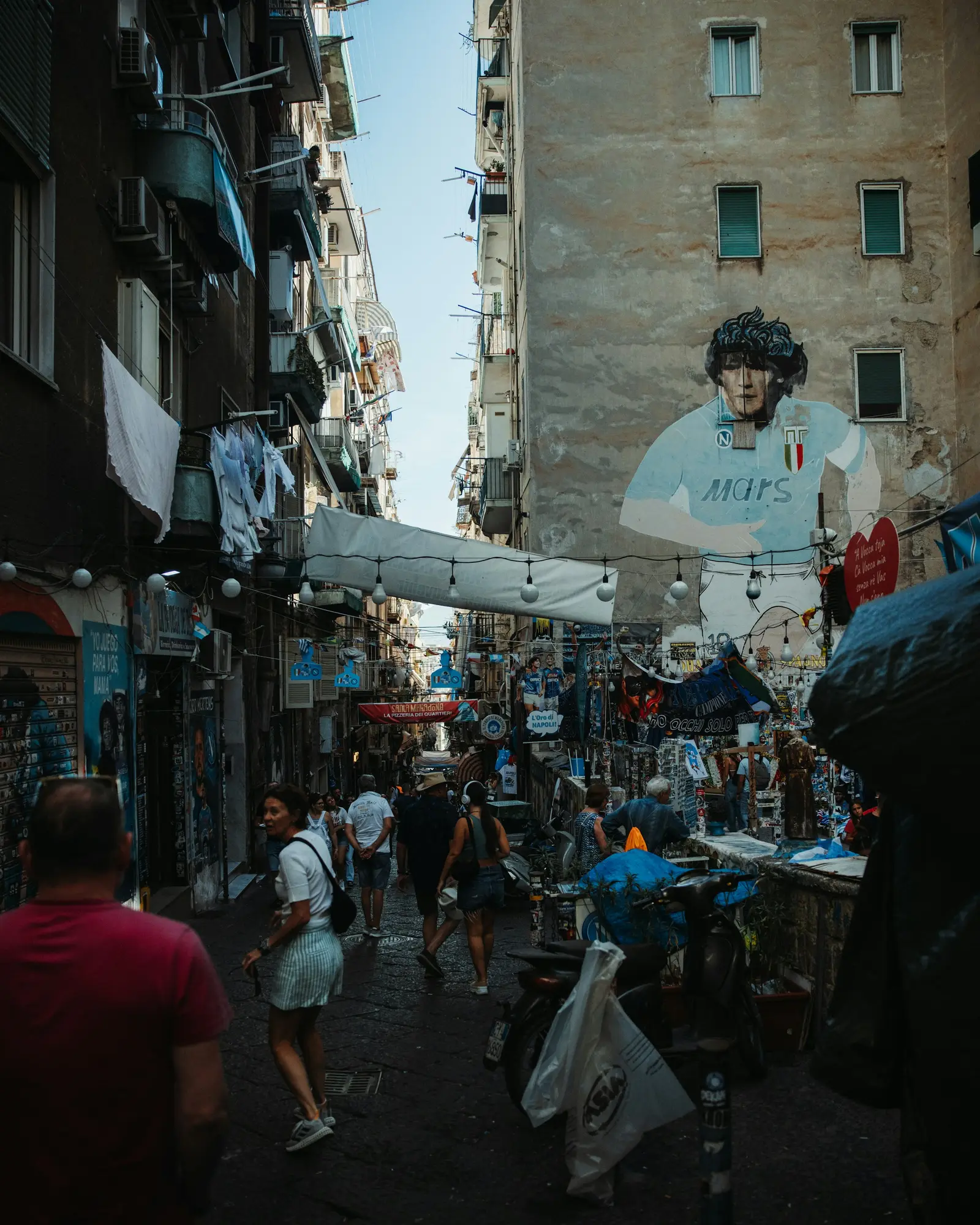 A lively Naples alley with scooters, pedestrians and a Maradona mural